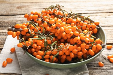 Photo of Fresh sea buckthorn berries with leaves in bowl on wooden table, closeup