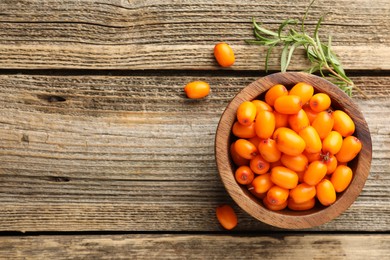 Photo of Fresh sea buckthorn berries in bowl and leaves on wooden table, flat lay. Space for text