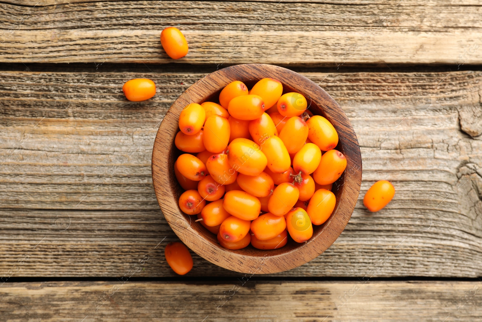 Photo of Fresh sea buckthorn berries in bowl on wooden table, top view