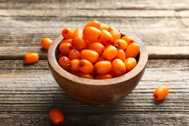 Photo of Fresh sea buckthorn berries in bowl on wooden table, closeup