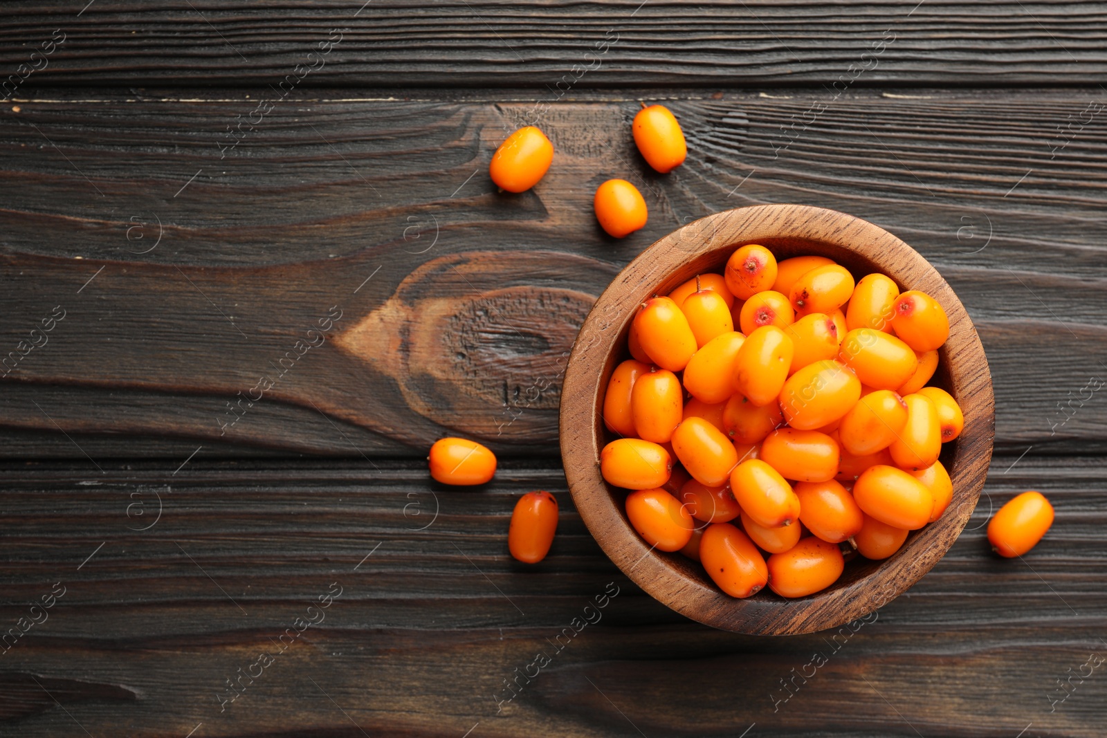Photo of Fresh sea buckthorn berries in bowl on wooden table, flat lay. Space for text