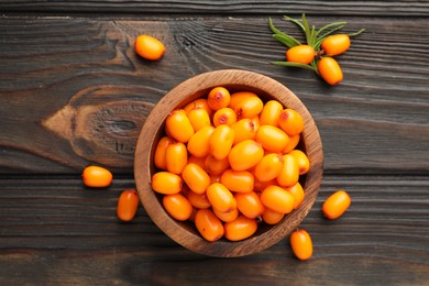 Photo of Fresh sea buckthorn berries in bowl and leaves on wooden table, flat lay