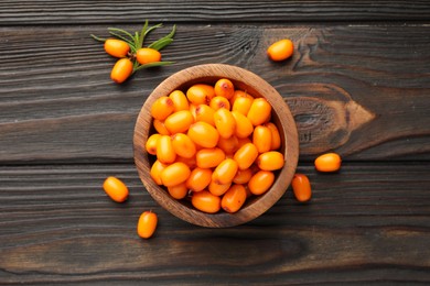 Photo of Fresh sea buckthorn berries in bowl and leaves on wooden table, flat lay