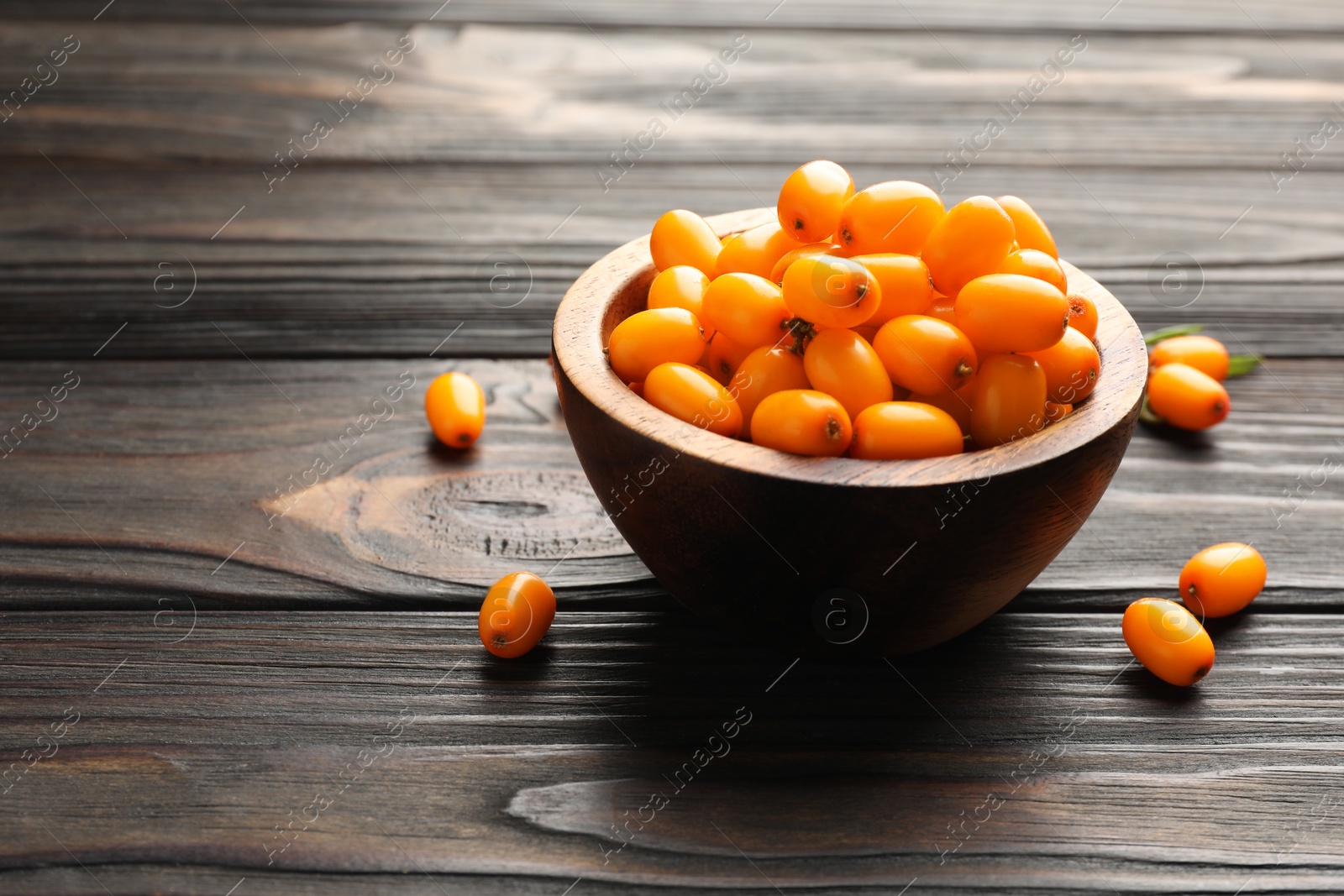 Photo of Fresh sea buckthorn berries in bowl on wooden table, closeup. Space for text