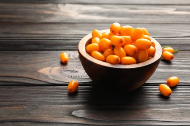 Photo of Fresh sea buckthorn berries in bowl on wooden table, closeup. Space for text