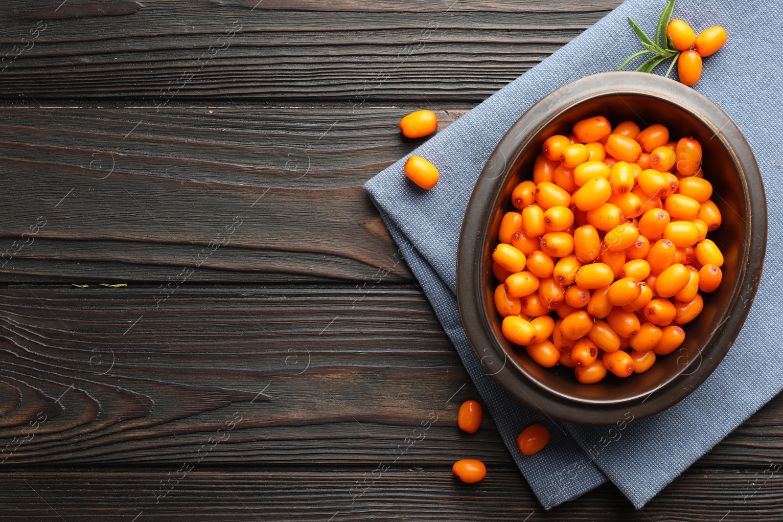 Photo of Fresh sea buckthorn berries in bowl and leaves on wooden table, flat lay. Space for text