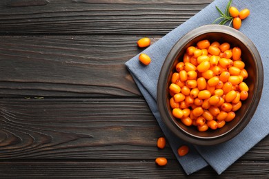 Photo of Fresh sea buckthorn berries in bowl and leaves on wooden table, flat lay. Space for text