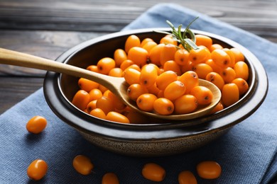 Photo of Fresh sea buckthorn berries in bowl and leaves on wooden table, closeup