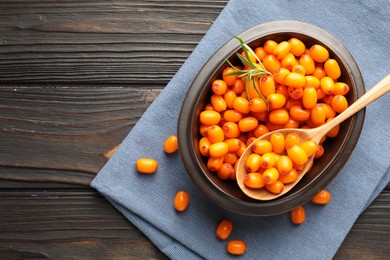 Photo of Fresh sea buckthorn berries in bowl and leaves on wooden table, flat lay. Space for text