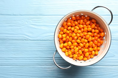 Photo of Fresh sea buckthorn berries in metal colander on light blue wooden table, top view. Space for text