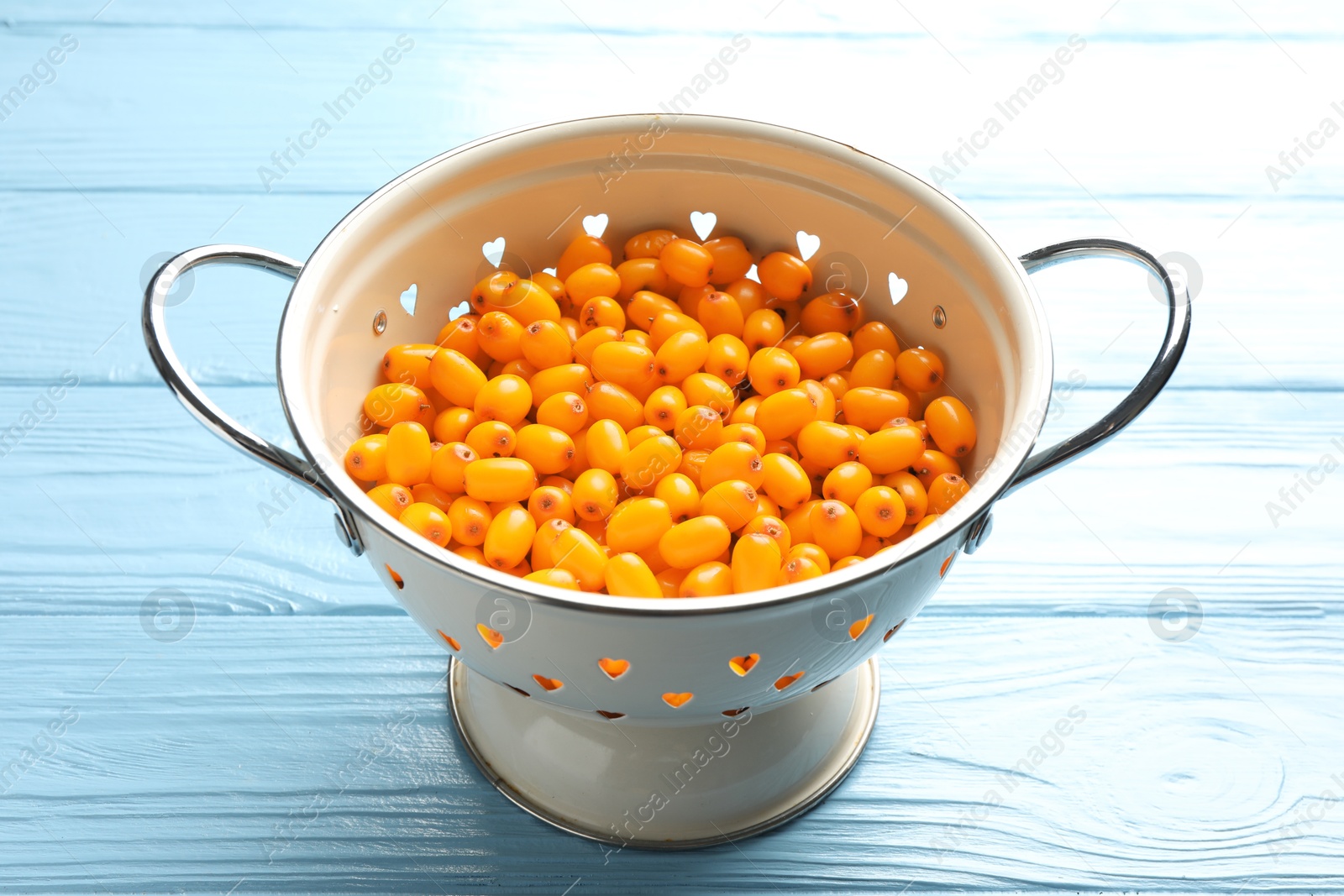 Photo of Fresh sea buckthorn berries in metal colander on light blue wooden table, closeup