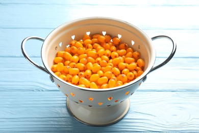 Photo of Fresh sea buckthorn berries in metal colander on light blue wooden table, closeup