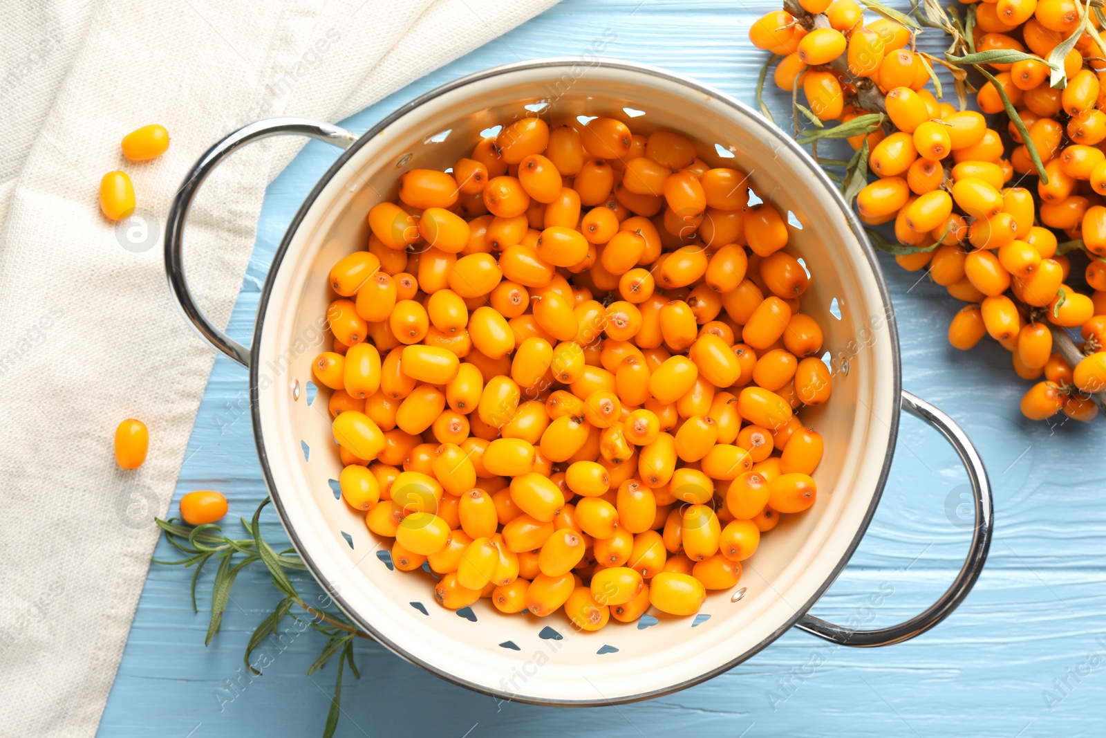 Fresh sea buckthorn berries in metal colander and leaves on light blue wooden table, flat lay Photo of Fresh sea buckthorn berries in metal colander and leaves on light blue wooden table, flat lay