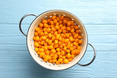 Photo of Fresh sea buckthorn berries in metal colander on light blue wooden table, top view