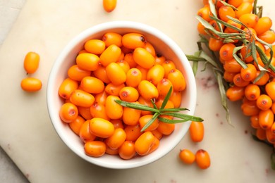 Photo of Fresh sea buckthorn berries in bowl and leaves on beige table, flat lay