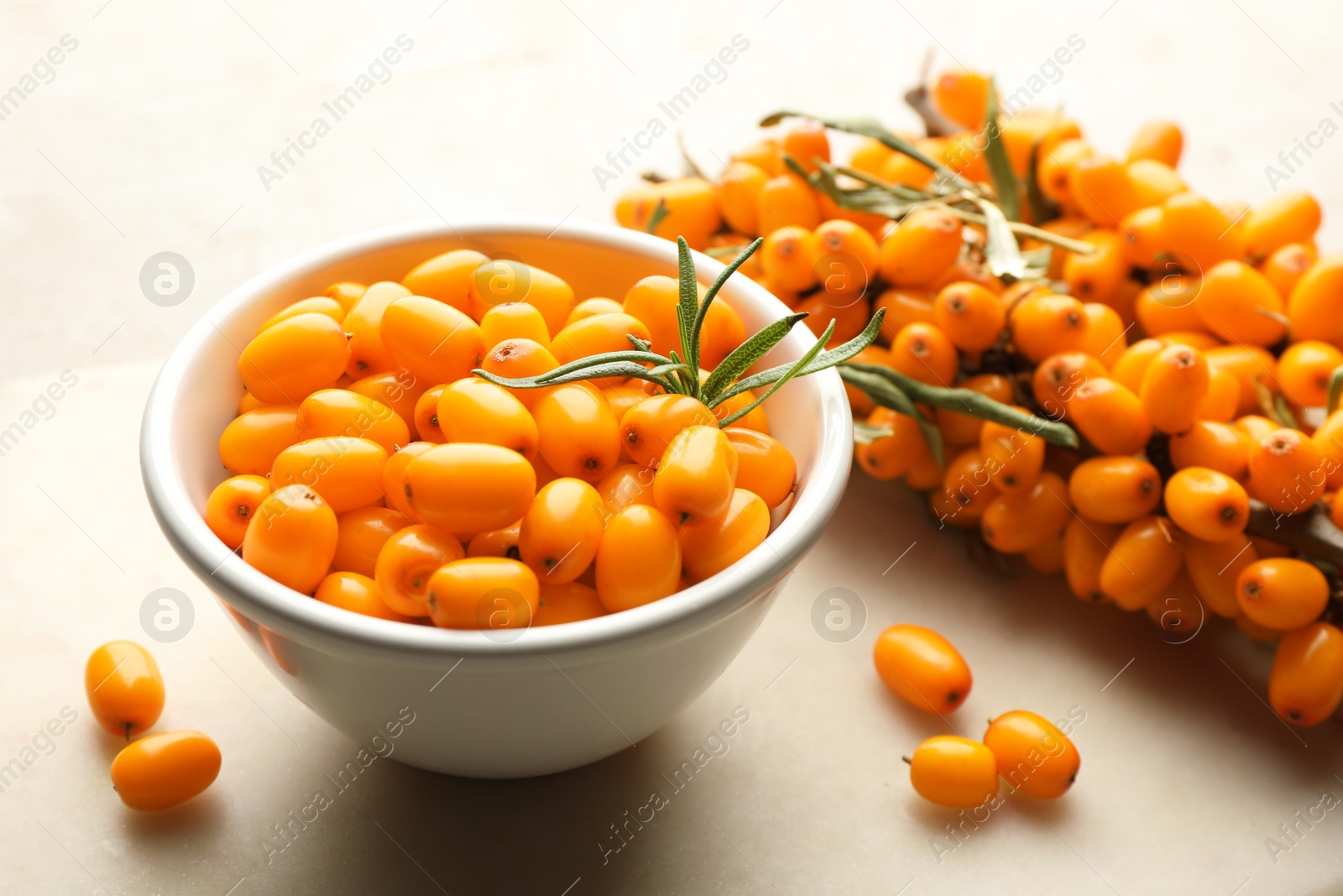 Fresh sea buckthorn berries in bowl and leaves on beige table, closeup Photo of Fresh sea buckthorn berries in bowl and leaves on beige table, closeup