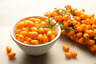 Photo of Fresh sea buckthorn berries in bowl and leaves on beige table, closeup
