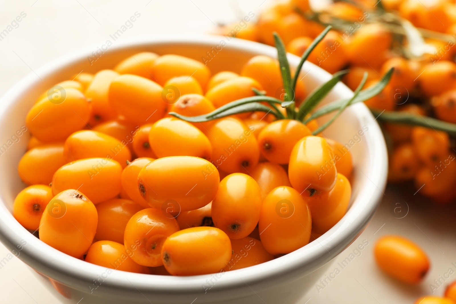 Fresh sea buckthorn berries in bowl and leaves on beige table, closeup Photo of Fresh sea buckthorn berries in bowl and leaves on beige table, closeup