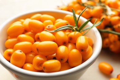 Photo of Fresh sea buckthorn berries in bowl and leaves on beige table, closeup