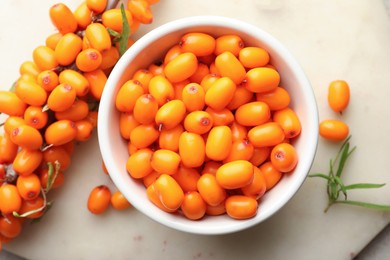 Photo of Fresh sea buckthorn berries in bowl and leaves on beige table, flat lay