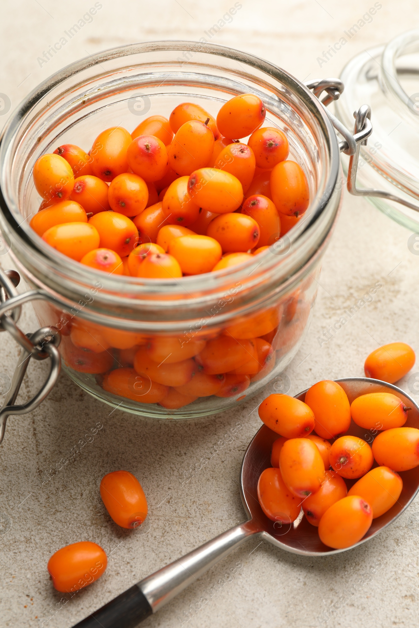 Photo of Fresh sea buckthorn berries in glass jar on beige table, closeup