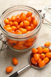 Photo of Fresh sea buckthorn berries in glass jar on beige table, closeup