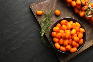Photo of Fresh sea buckthorn berries with leaves in bowl on black table, top view. Space for text