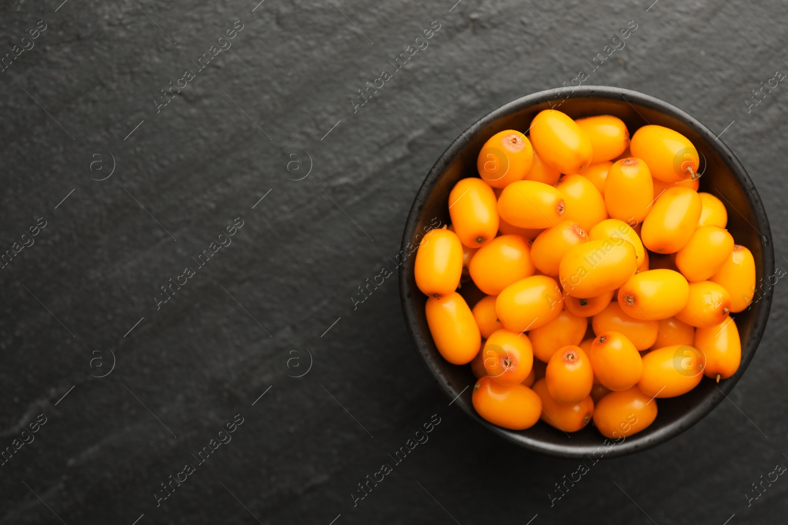 Photo of Fresh sea buckthorn berries in bowl on black table, top view. Space for text