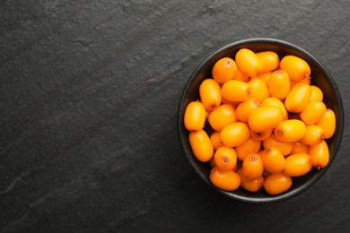 Photo of Fresh sea buckthorn berries in bowl on black table, top view. Space for text