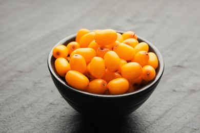 Photo of Fresh sea buckthorn berries in bowl on black table, closeup
