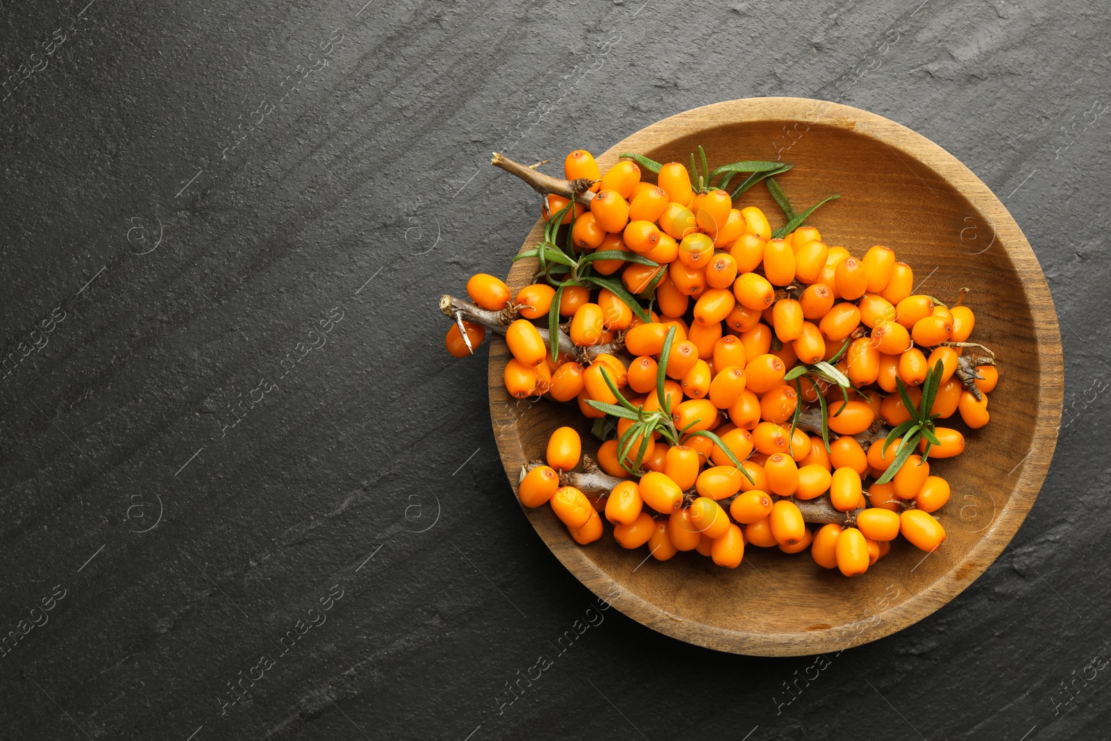 Photo of Fresh sea buckthorn berries with leaves in bowl on black table, top view. Space for text