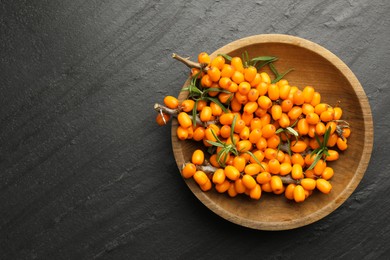 Photo of Fresh sea buckthorn berries with leaves in bowl on black table, top view. Space for text