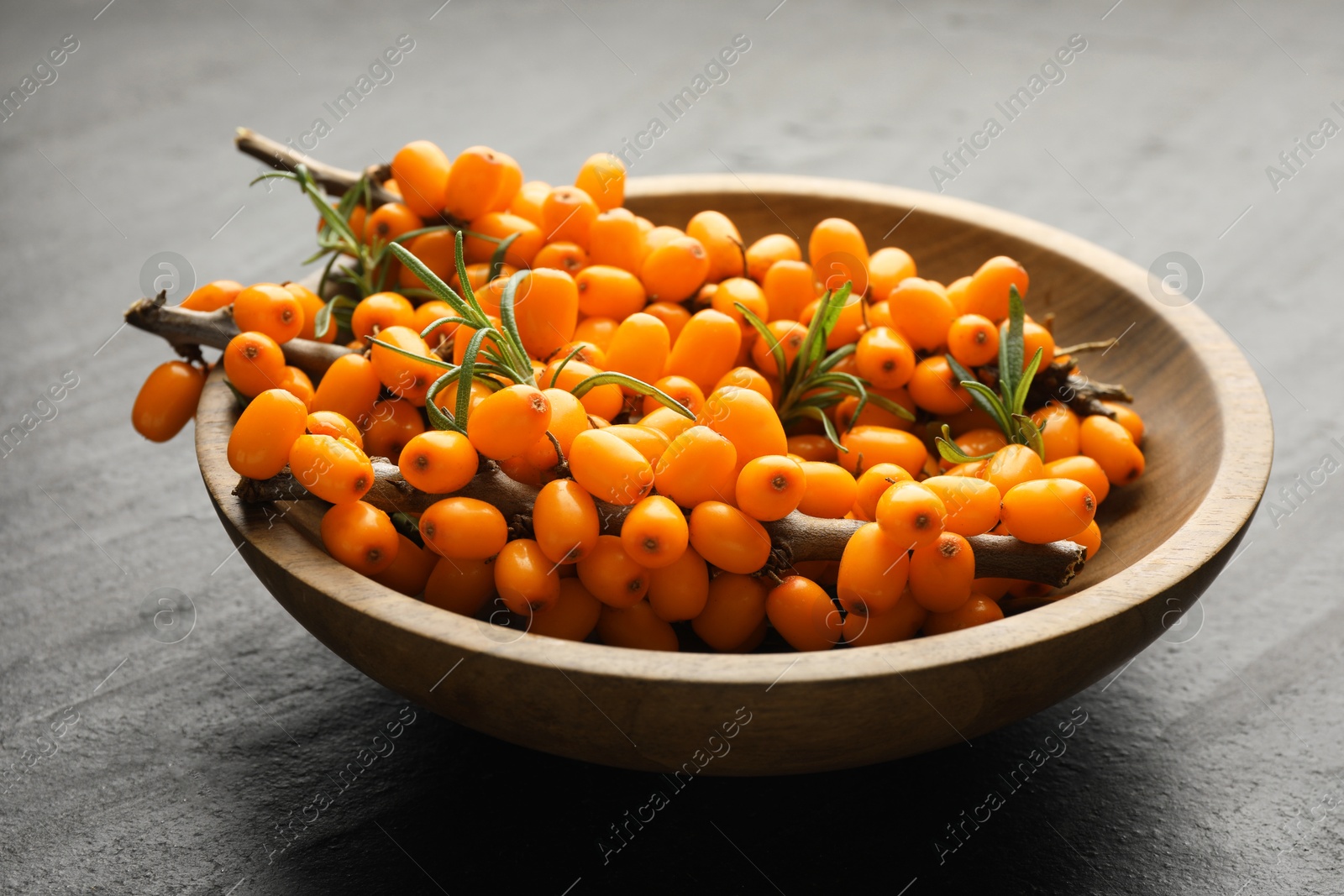 Photo of Fresh sea buckthorn berries with leaves in bowl on black table, closeup