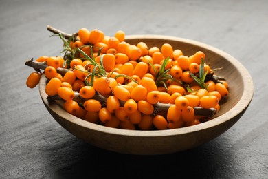Photo of Fresh sea buckthorn berries with leaves in bowl on black table, closeup