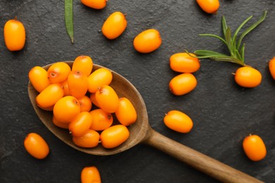 Photo of Fresh sea buckthorn berries, spoon and leaves in on black table, flat lay
