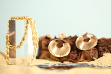Photo of Beautiful gold jewelry and wood on sand, closeup. Space for text