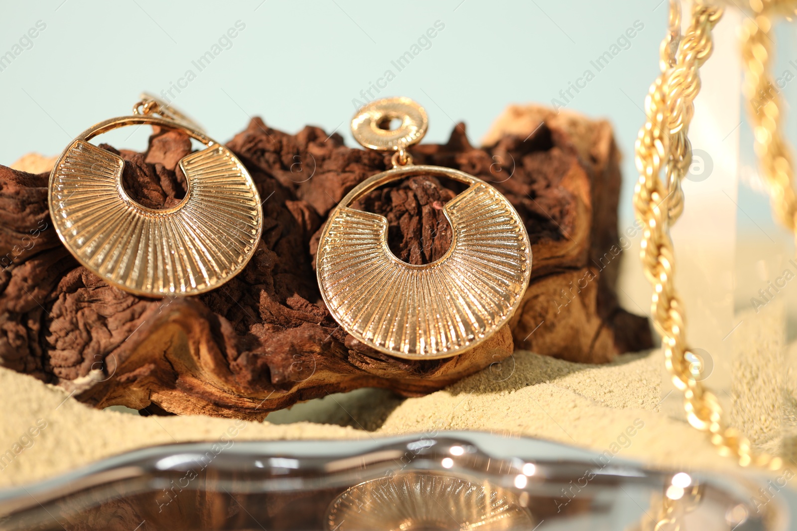 Photo of Beautiful gold jewelry and wood on sand, closeup