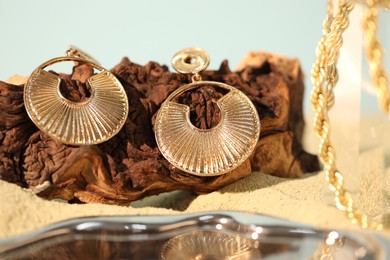 Photo of Beautiful gold jewelry and wood on sand, closeup