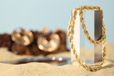 Photo of Beautiful gold chain on sand, closeup. Space for text