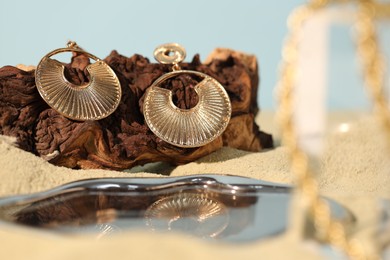 Photo of Beautiful gold earrings and wood on sand, closeup