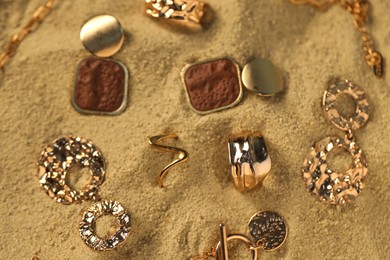 Photo of Different beautiful gold jewelry on sand, closeup