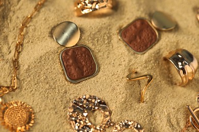 Photo of Different beautiful gold jewelry on sand, closeup
