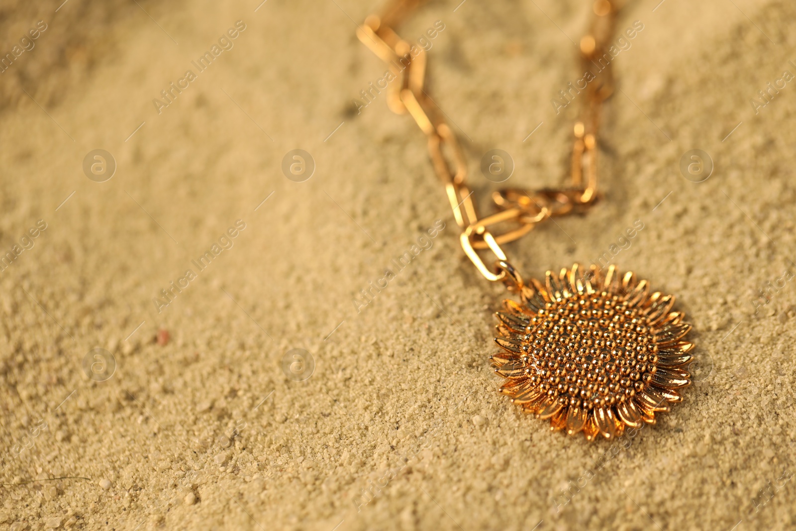 Photo of Beautiful gold necklace on sand, closeup. Space for text