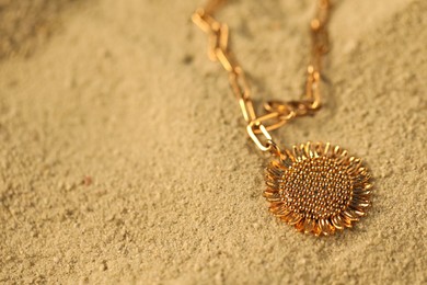 Photo of Beautiful gold necklace on sand, closeup. Space for text