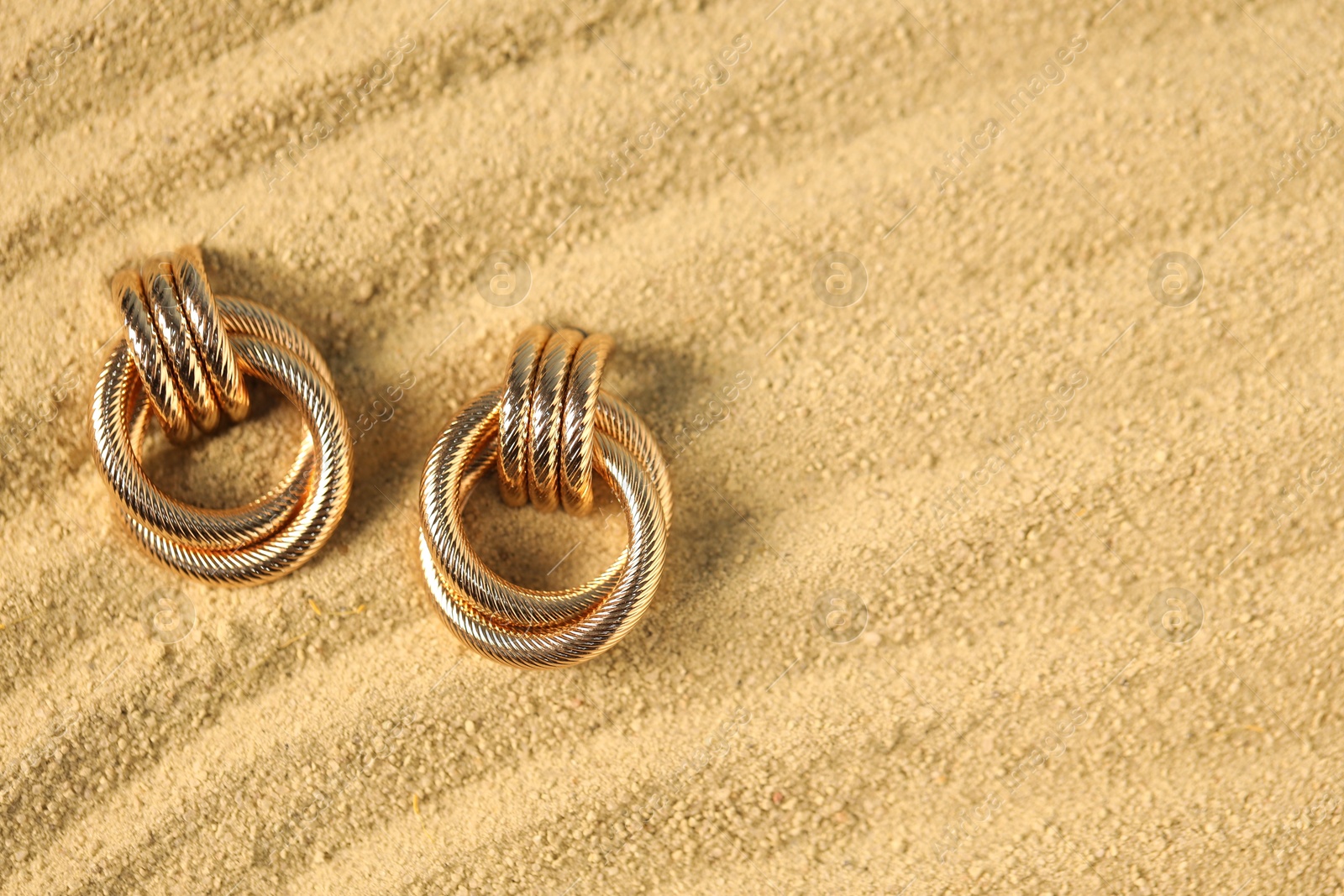 Photo of Beautiful gold earrings on sand, flat lay. Space for text