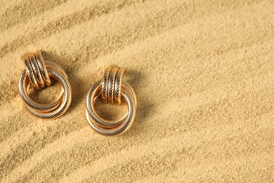 Photo of Beautiful gold earrings on sand, flat lay. Space for text
