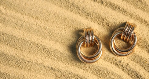 Photo of Beautiful gold earrings on sand, flat lay. Space for text
