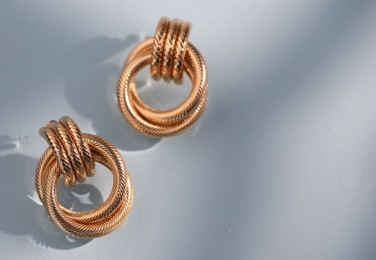 Photo of Beautiful gold earrings on light blue background, closeup. Space for text