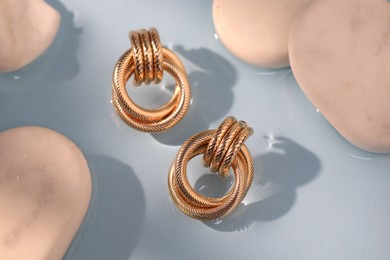 Photo of Beautiful gold earrings and rocks in water on light blue background, closeup