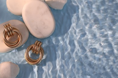 Photo of Beautiful gold earrings and rocks in water on light blue background, closeup. Space for text